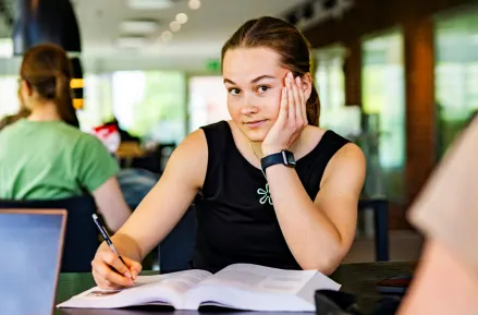 Student med bok tittar in i kameran. Foto.