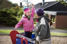 Ett barn och en äldre vuxen tillsammans på en lekplats. De ser glada ut.