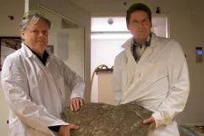 Två manliga forskare i vita rockar håller en sten.