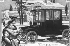 Gammal annons för elektrisk bil. En teckning där en snyggt klädd kvinna tittar på en bil. Texten: One of our rare creations for 1912.