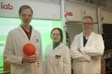 Tre kemiforskare i vita rockar framför ett dragskåp.