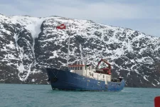 Bild på blått forskningsfartyg med arktiska berg i bakgrunden.