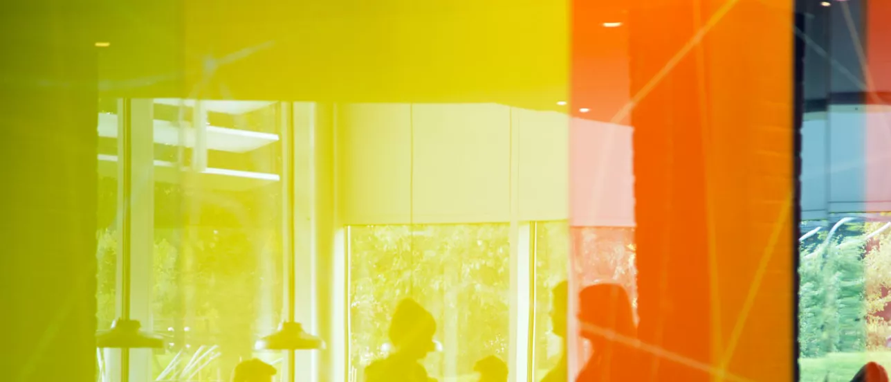 Närbild gul och orange glasvägg som speglar några studenter. Foto.
