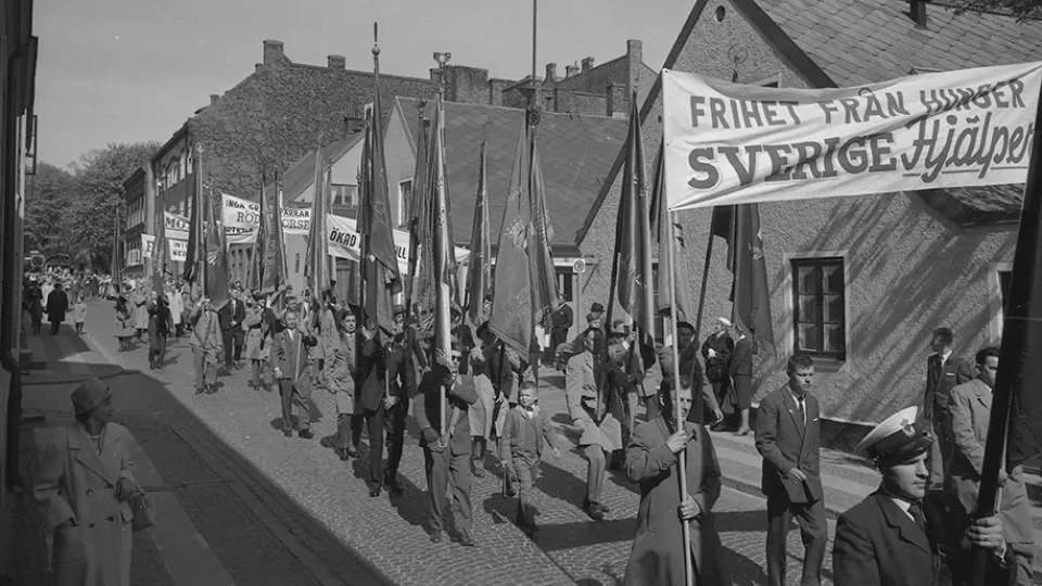 Personer går med banderoller och fanor på en gata i Lund 1963. Troligen en första maj-demonstration. Foto.