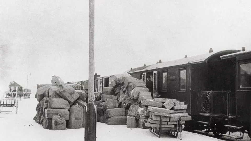 Paket i en stor hög på perrongen bredvid ett tåg i början av 1900-talet.