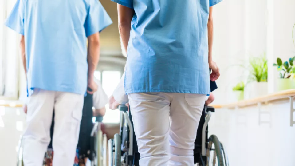 Skötare leder fram personer som sitter i rullstol
