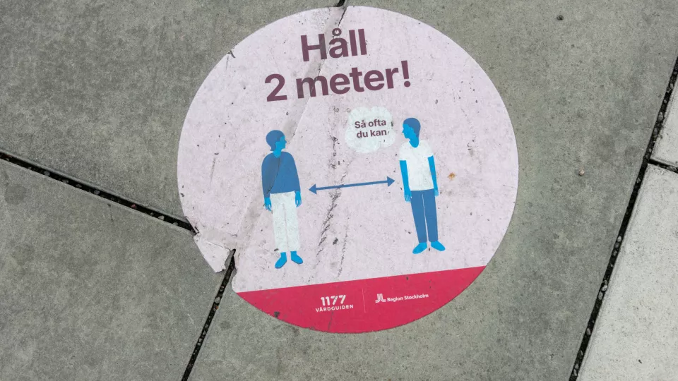Bild på en skylt som säger att man ska hålla två meter avstånd till varandra
