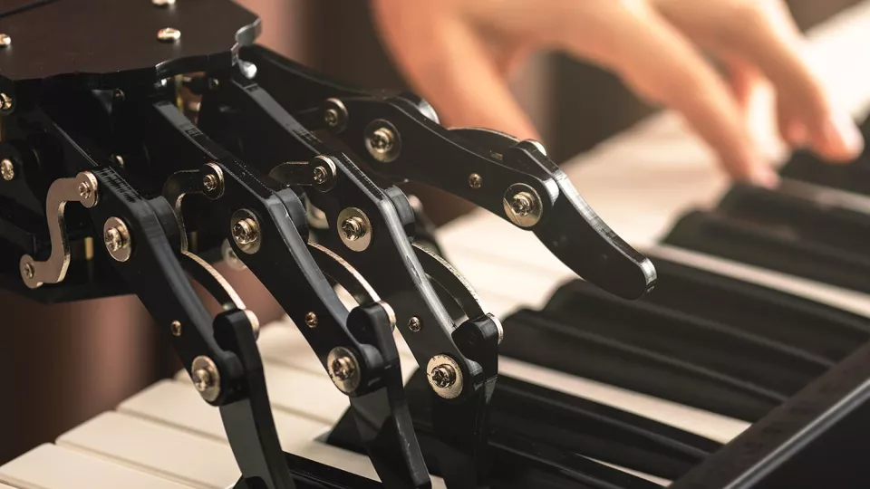 En robothand och en mänsklig hand som spelar på ett piano, sida vid sida. Foto.