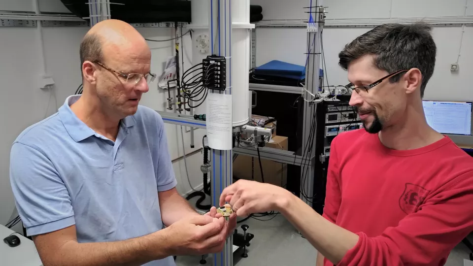 Två manliga forskare visar upp en detektor i ett laboratorium.