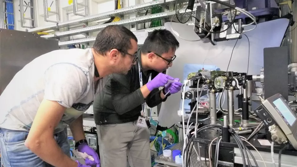 Två forskare studerar en analysapparat i ett laboratorium.