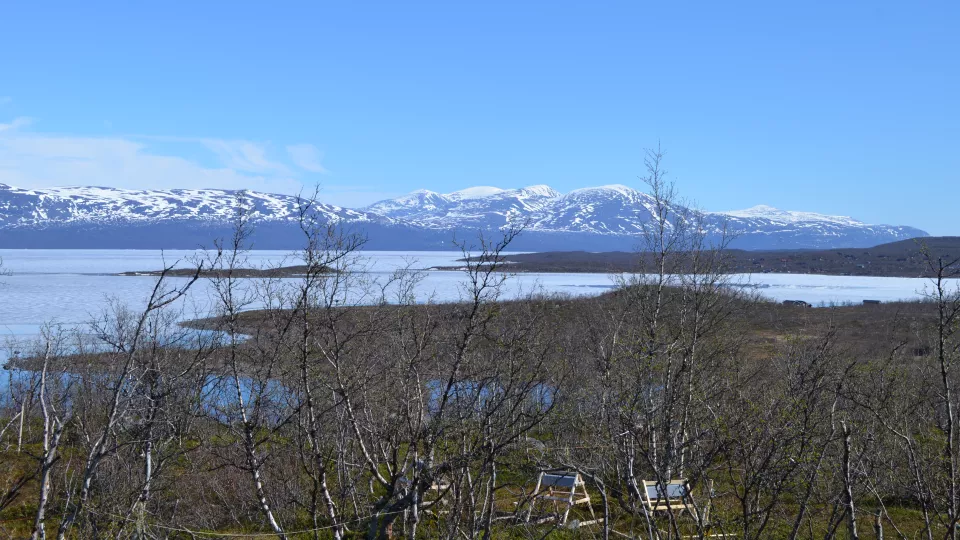 Bild på landskap med sjö och snöklädda berg. Foto