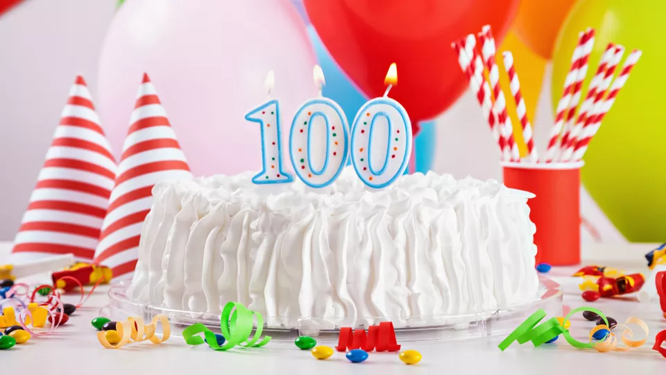 Tårta med 100-årsljus och ballonger. Foto. 