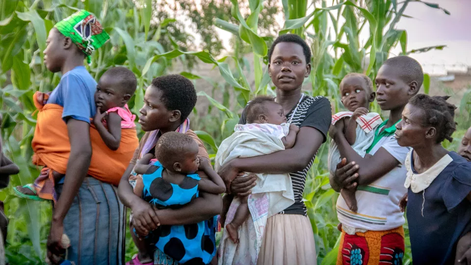 Foto. Flera kvinnor i Uganda står står uppradade tillsammans med sina barn som de bär i famnen eller på ryggen.
