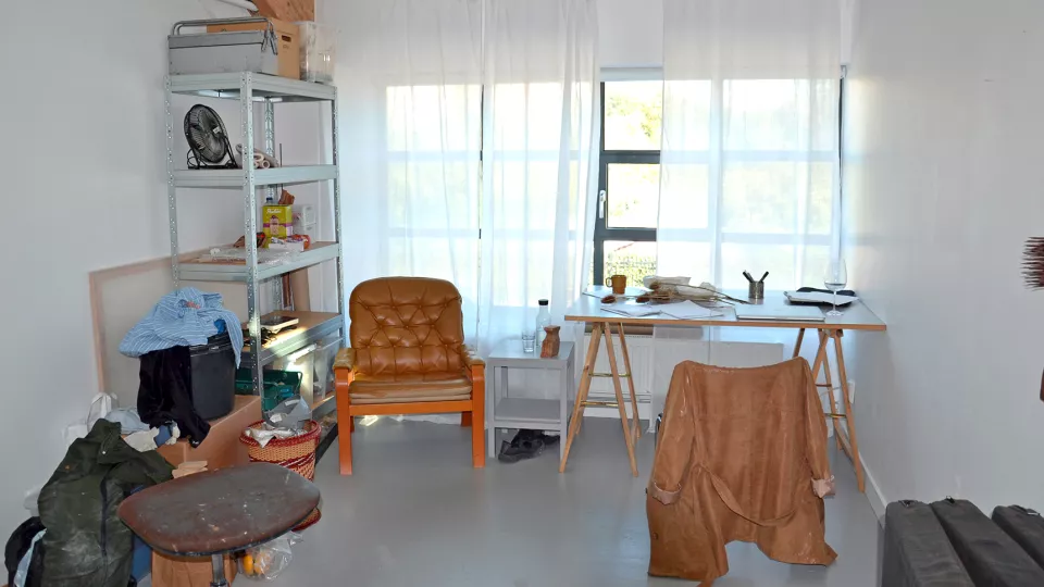 Foto inifrån en ateljé på Konsthögskolan i Malmö, med stolar, skrivbord och konstnärsmaterial.