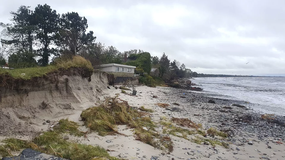 Eroderad strand med hus med bortspolad grund. Foto.