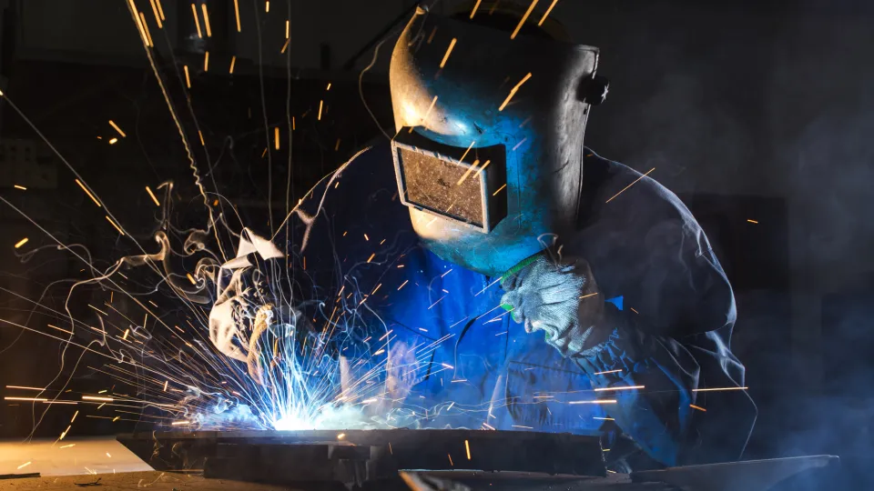 Man med skyddsutrustning svetsar, eldflugor sprätter iväg, fotografi. Foto: iStock/posonsky
