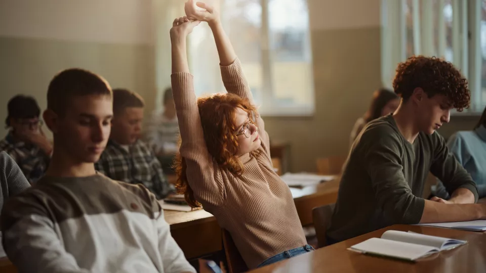 Tonårstjej i klassrum sträcker på sig, fotografi. Foto: iStock