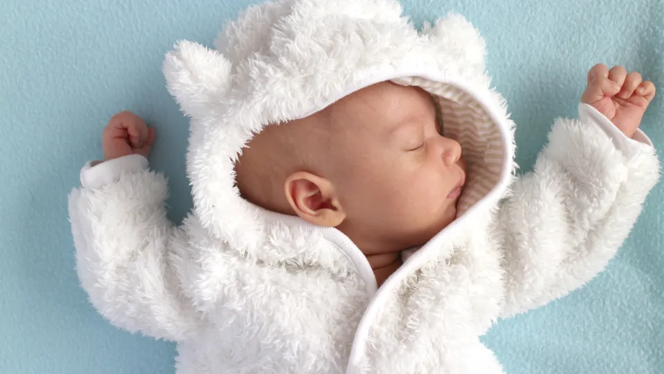 Bebis i teddyoverall mot blå bakgrund, fotografi. Foto: iStock