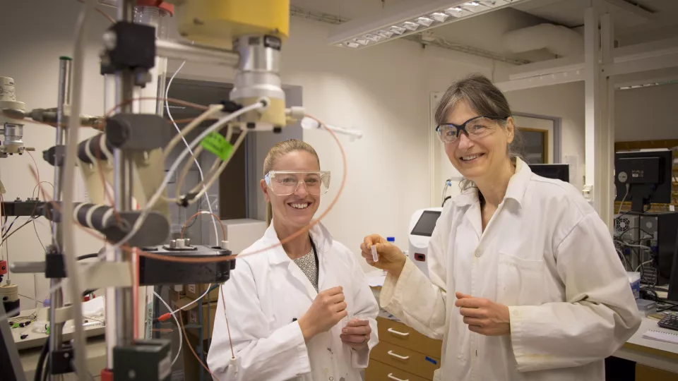 Två kvinnliga forskare i vita rockar i laboratorium.