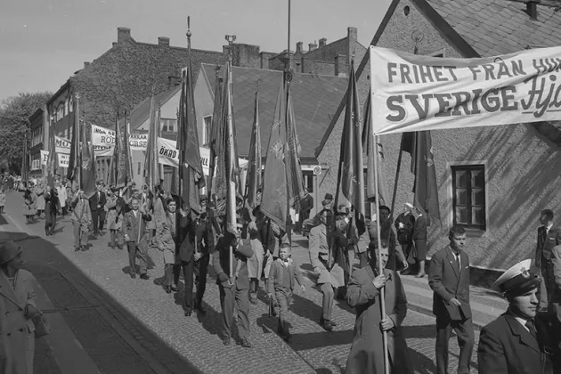 Personer går med banderoller och fanor på en gata i Lund 1963. Troligen en första maj-demonstration. Foto.
