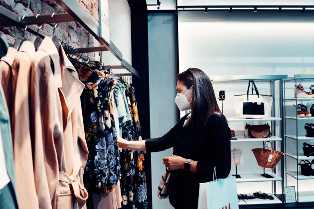 Kvinna med munskydd tittar på kläder i en butik. Foto.
