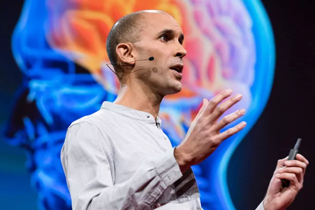 Photo of a man giving a lecture in front of an illustration of a human brain.