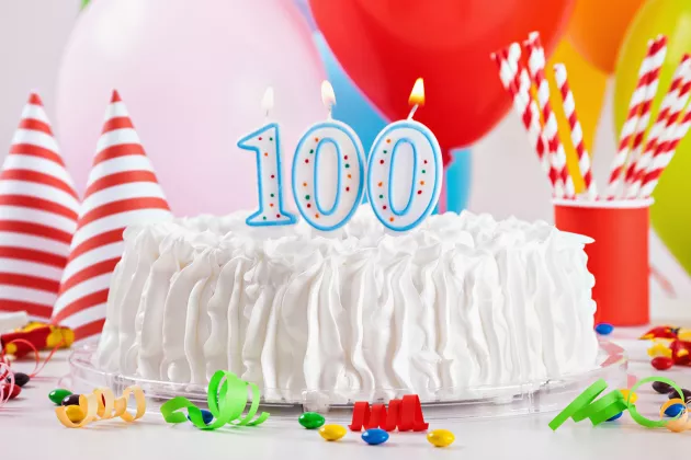 Tårta med 100-årsljus och ballonger. Foto. 