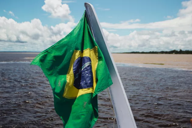 Den brasilianska flaggan som hålls upp på en båt i Amazonas. Bild: Unsplash.