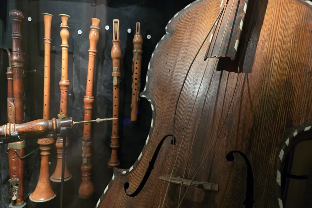 I förgrunden ses en del av en cello. Bakom hänger olika sorters träblåsinstrument uppradade.