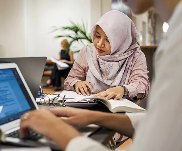 Student sitter och läser en bok i en läs-sal med andra. Foto: Johan Persson.