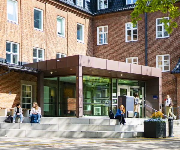 Personer sitter på trappan framför byggnaden Gamla köket. Foto.