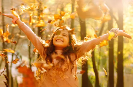 Glad tjej kastar upp löv i luften. Foto.