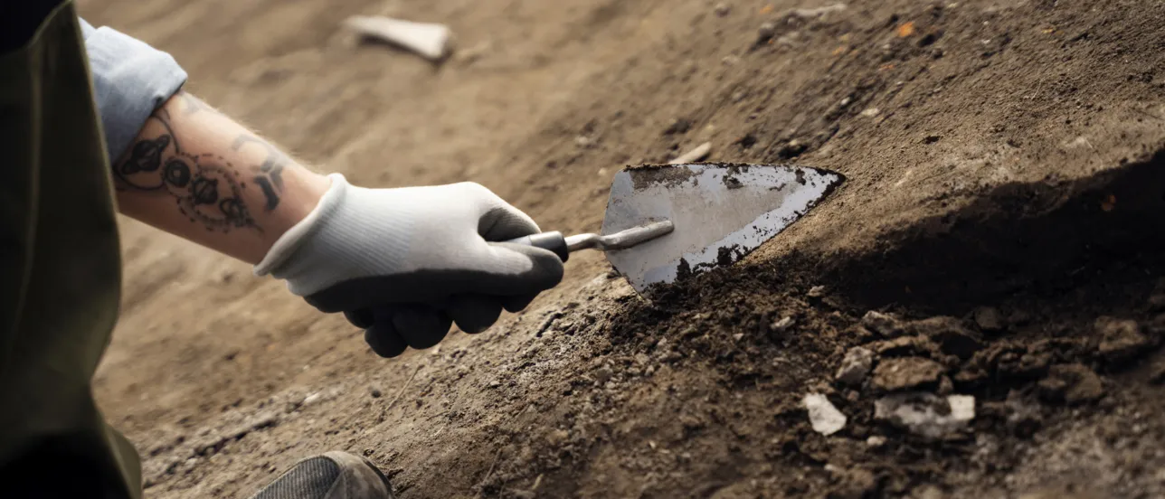 En hand med handske håller i en spade och gräver i jorden.