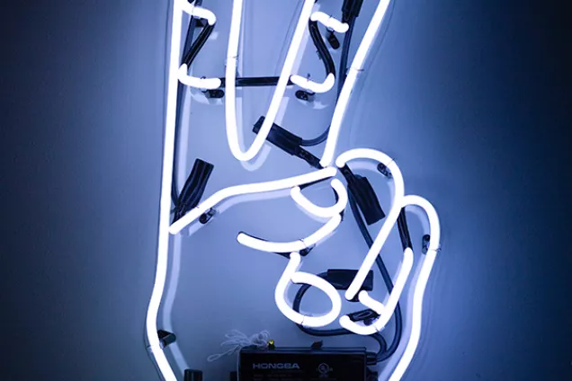 Neonskylt med hand som gör segertecken. Foto.
