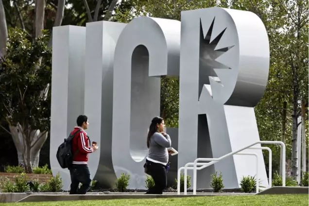 Två studenter passerar gigantiska bokstäver UCR "UC Riverside". Foto.
