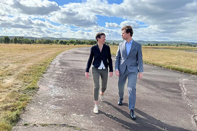 Två personer som promenerar på en asfalterad yta. Foto.
