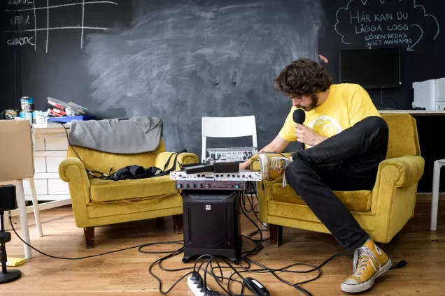 En student sänder radio, omgiven av teknik, i en gul fåtölj. Foto Kennet Ruona.