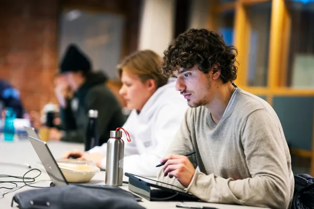 Fokuserad student läser på en laptop och tar anteckningar med en surfplatta. Foto :Johan Persson.