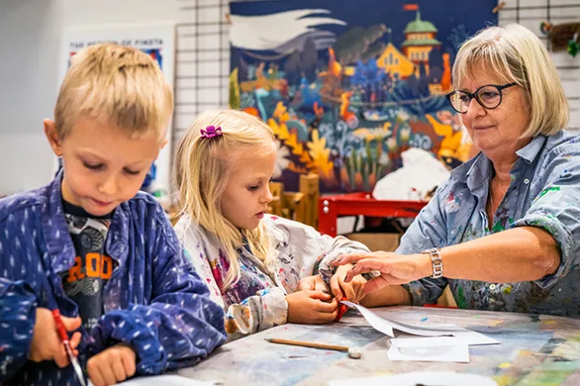 Skapande-verkstaden-2462-Johan-Persson.jpg Två barn sitter vid ett bord och pysslar tillsammans med en vuxen.