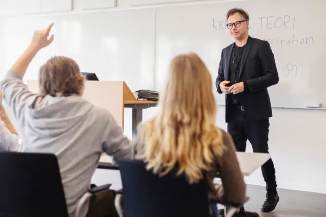 Två studenter och en lärare vid whiteboard. Foto.