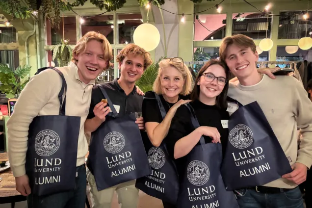 Fem glada alumner med universitetskassar. Foto.