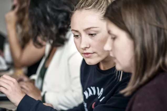 Två kvinnliga studenter sitter och studerar inomhus.