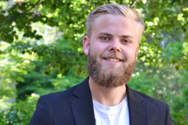 Emil står utomhus bland träd och ler in i kameran.