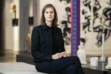 Museichef Annie Lindberg sitter på en bänk inne i Skissernas museum bland olika skulpturer och föremål. Hon är klädd i svart och tittar in i kameran.