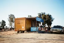 Photo of a shack placed on sandy, dry ground. A car is parked to the right of the shack.