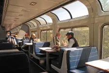 People sitting in a train car, looking out of big windows over woods.