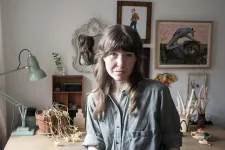 Konstnären Clara Dackenberg. I bakgrunden tavlor med illustrationer, lampa, skulpturer. 