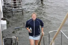 Foto på Isabel Erb som går upp från havet med ett flaska med havsvatten i handen