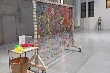 Ett stort nät är uppspänt på en träram. I nätet färgglada garntrådar.