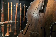 I förgrunden ses en del av en cello. Bakom hänger olika sorters träblåsinstrument uppradade.